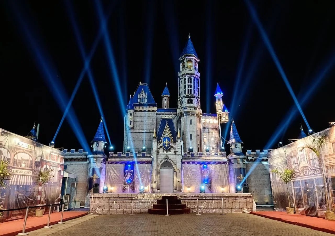 Castelo iluminado com feixes de luz no céu, à noite