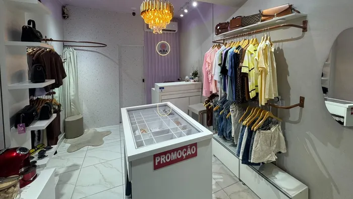 Araras de roupas, prateleiras com bolsas e o lustre de cristal no salão da Aura Choice