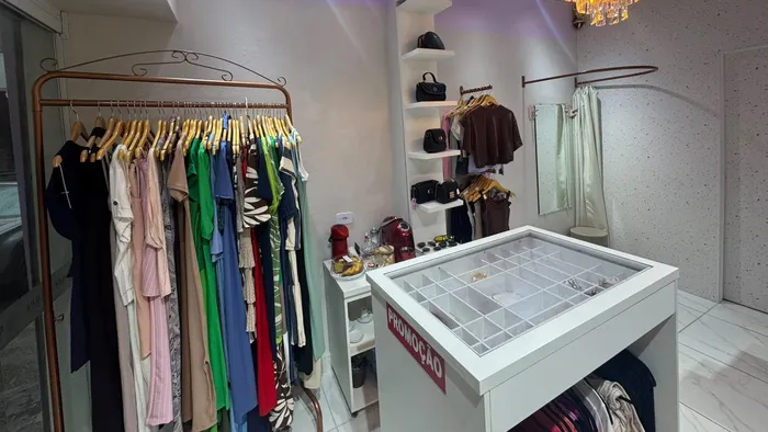Arara de cobre com vestidos e blusas coloridas ao lado do balcão de acessórios da Aura Choice