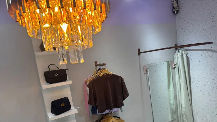 Prateleiras de bolsas, peças marrons penduradas e o provador da Aura Choice sob o lustre