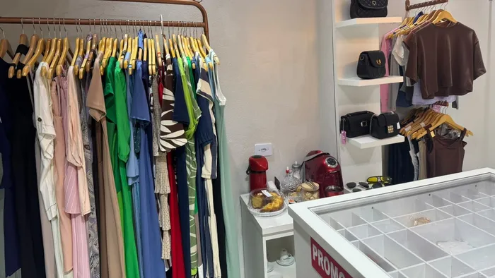 Arara com vestidos e blusas em várias cores e prateleira de bolsas na Aura Choice