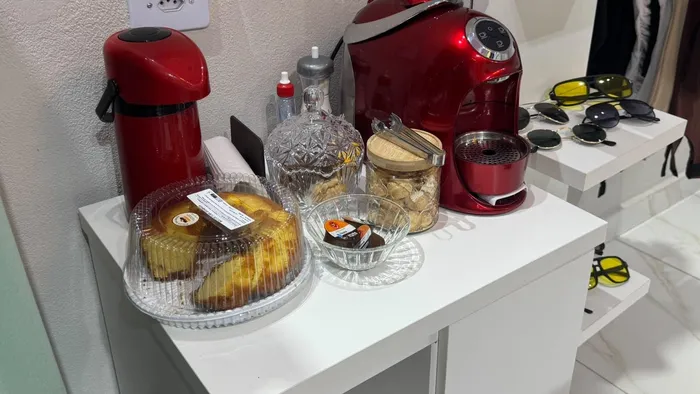 Cantinho do café da Aura Choice, com garrafa térmica, cafeteira vermelha e bolo para as clientes