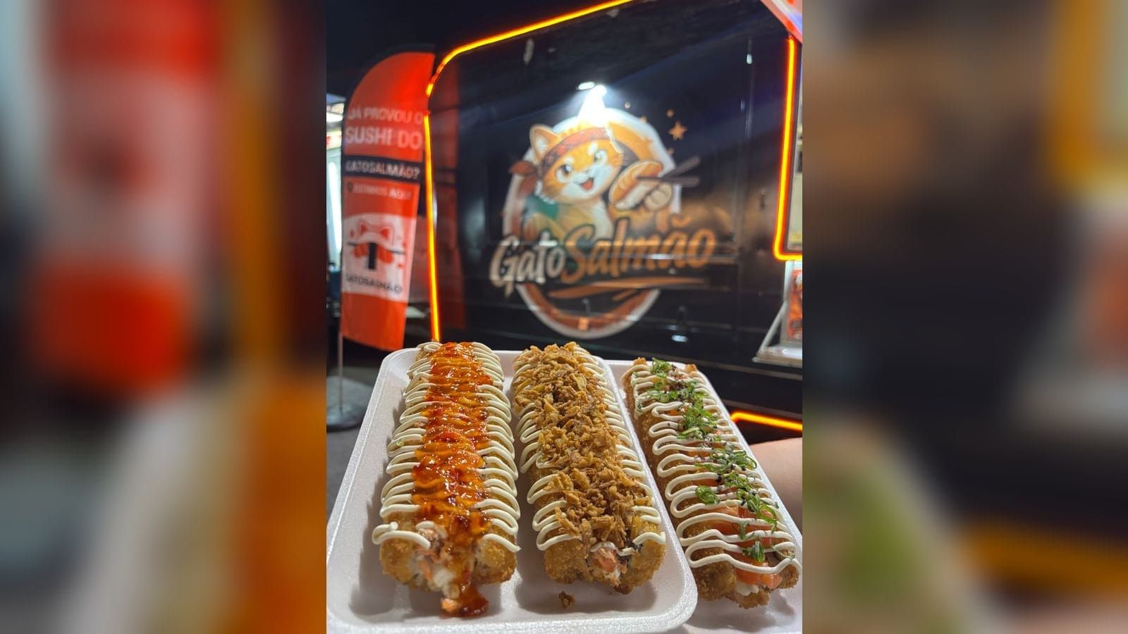 Três Big Hots empanados, com cobertura de molho de pimenta, cebola crispy e cebolinha, na frente do food truck Gatosalmão