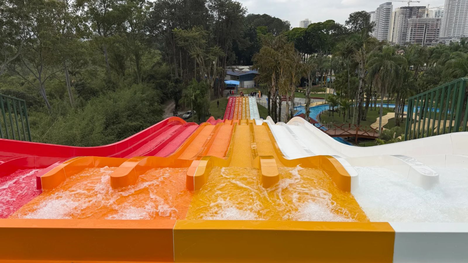 As oito pistas coloridas do Turbogã, em vermelho, laranja, amarelo e branco, vistas do alto da largada, com a mata do Thermas do Vale e prédios ao fundo