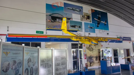 Salão interno do Memorial Aeroespacial Brasileiro com um avião amarelo suspenso, painéis sobre o ITA e vitrines de exposição