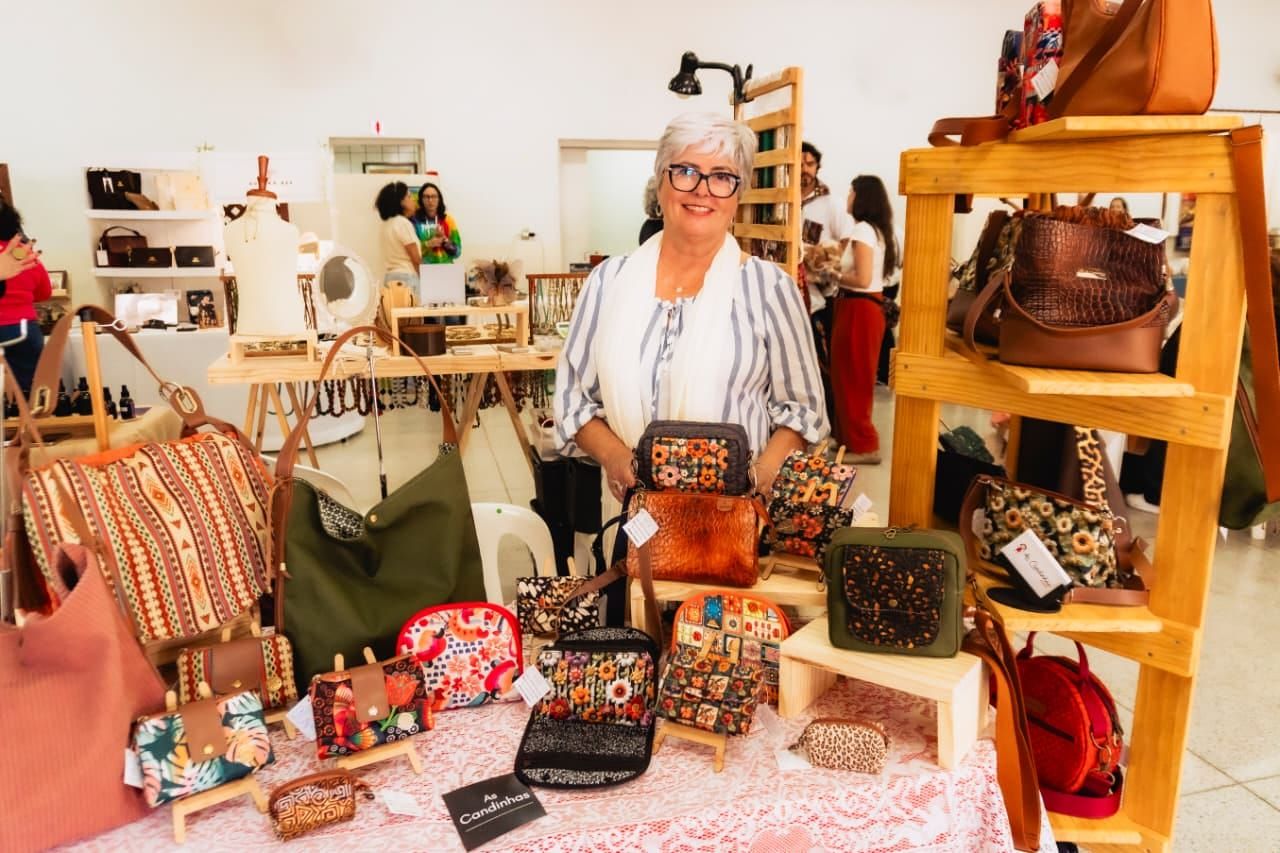 Expositora atrás da banca de bolsas artesanais em uma edição do Mercadinho Artesanal