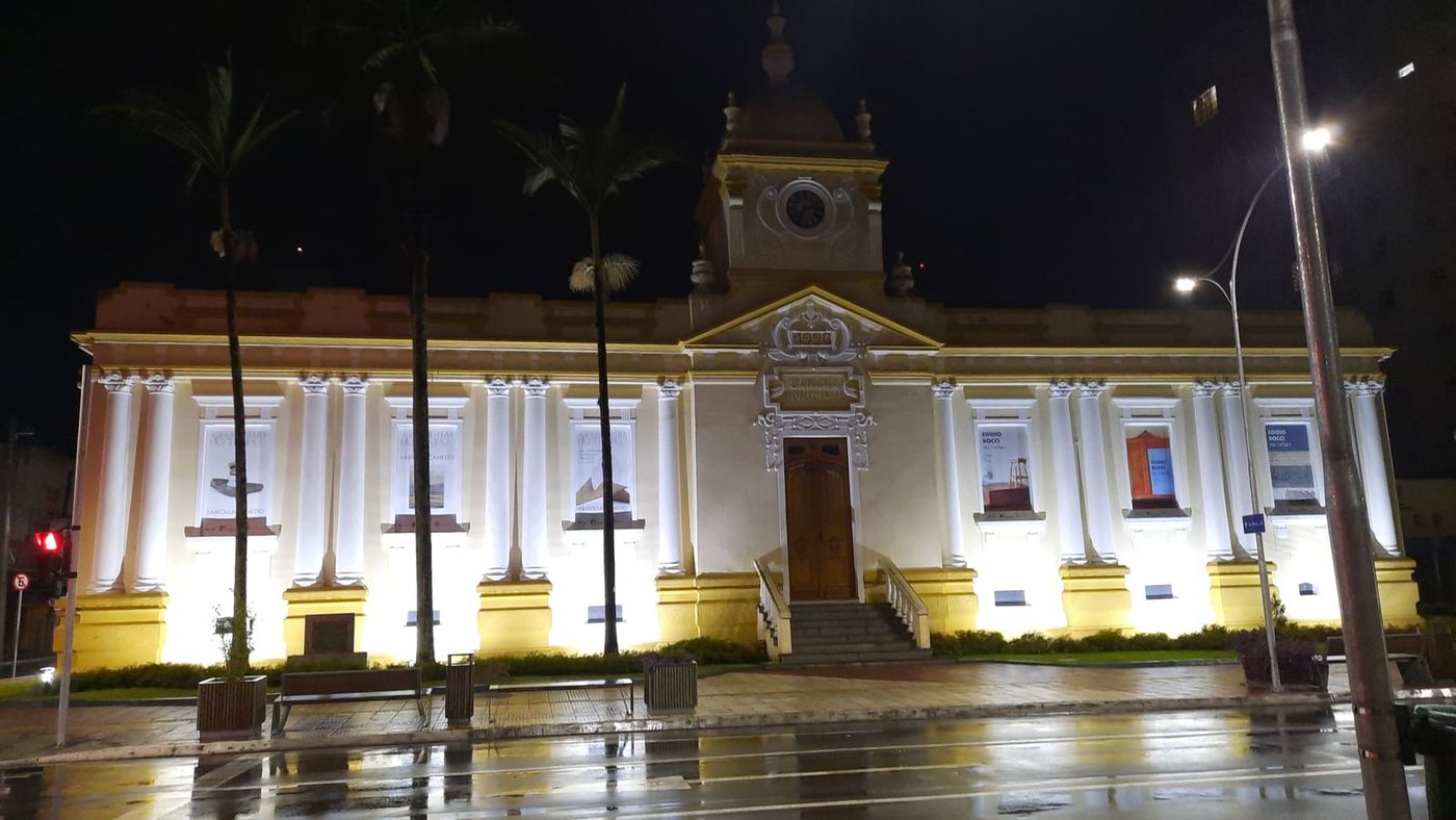 Fachada iluminada à noite do Museu Municipal de São José dos Campos, prédio da antiga Câmara com colunas, torre do relógio e banners de exposição nas janelas