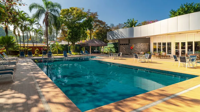 Piscina externa do Novotel São José dos Campos cercada de palmeiras e espreguiçadeiras