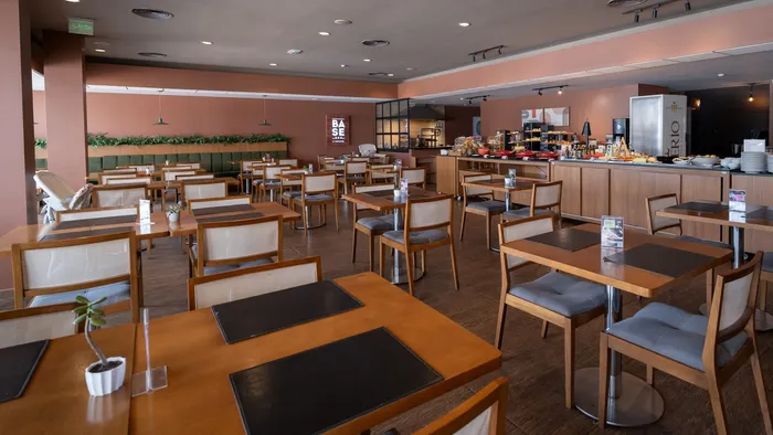 Salão do restaurante Base BBQ by Novotel, com mesas de madeira e buffet ao fundo