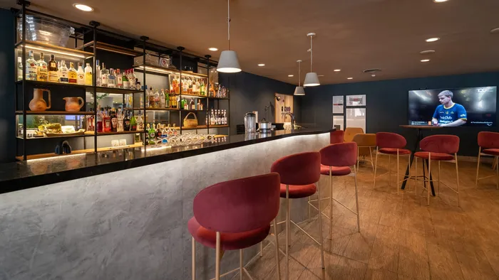 Bar do Novotel São José dos Campos, com balcão iluminado e banquetas vermelhas