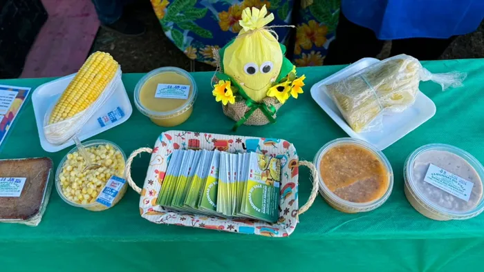 Mesa da Pamonhas do Vale com milho, curau, pamonha, bolo e um enfeite de espiga de milho