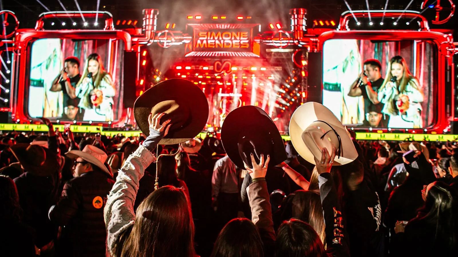 Público do Vale Rodeio Show ergue chapéus de cowboy diante do palco iluminado de vermelho, com Simone Mendes nos telões, em foto de edição anterior